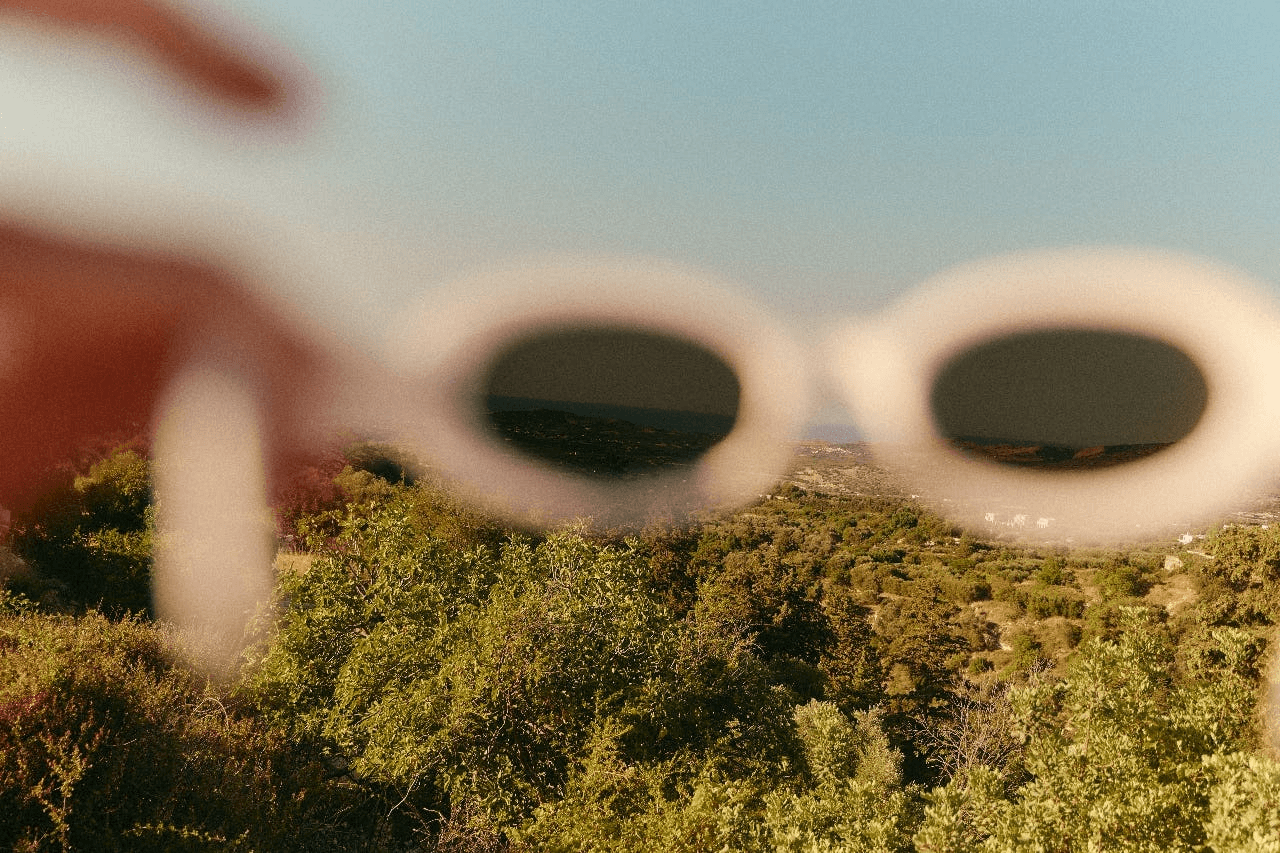 Hand holding sunglasses in front of a wide landscape.