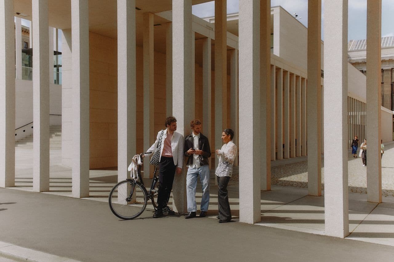 Three people in conversation between architectural columns in an open urban space